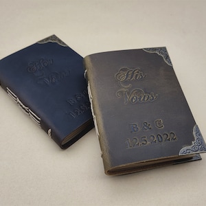 May include: Two small leather-bound journals with decorative metal corners. The covers are embossed with the words "Her Vows" and "His Vows" and the initials "B & C" and the date "12.5.2022".