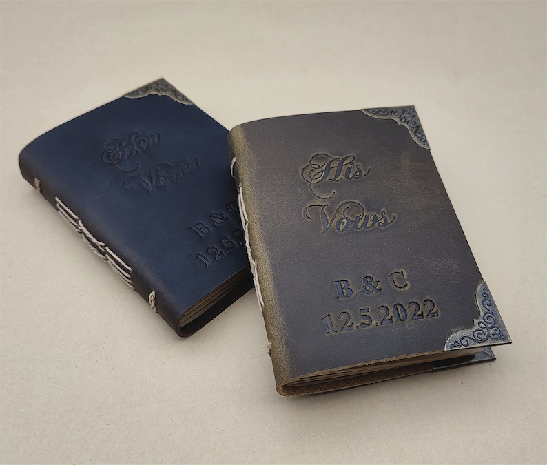 May include: Two small leather-bound journals with decorative metal corners. The covers are embossed with the words "Her Vows" and "His Vows" and the initials "B & C" and the date "12.5.2022".