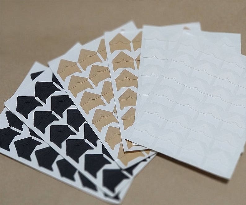 May include: A set of photo corner stickers in black, brown, and white. The stickers are in the shape of a corner and have a sticky back.