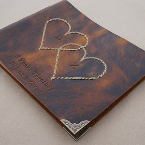 May include: A brown leather photo album with two stitched hearts and the text "5 Years Together Diana & Zoran". The album has decorative metal corners.