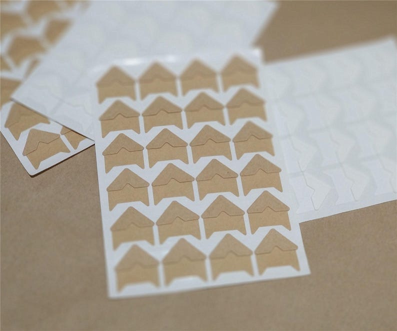 May include: A sheet of brown corner photo stickers with adhesive on the back. The stickers are arranged in a grid pattern on a white sheet.