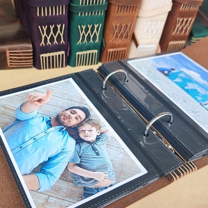 Può includere: Un album fotografico in pelle marrone con un raccoglitore ad anelli nero e argento. L'album è aperto per rivelare una foto di un padre e un figlio. La foto mostra il padre che indica qualcosa fuori campo, mentre il figlio guarda la fotocamera. L'album contiene anche una foto di una mappa del mondo.