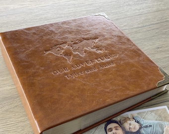 May include: A brown leather photo album with a world map design and the text "Our Adventures Tyler and Anna".
