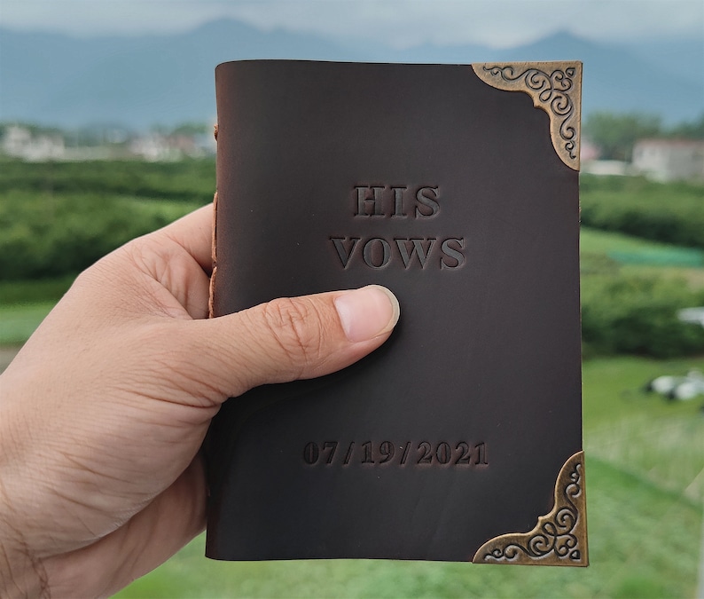 Puede incluir: Un diario de cuero marr&oacute;n con detalles dorados en las esquinas. La portada est&aacute; grabada con el texto "HIS VOWS" y la fecha "07/19/2021".