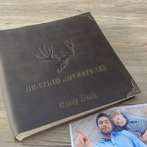 May include: A brown leather photo album with a deer head design and the text "Hunting Adventures" and "Casey Dark" embossed on the front.