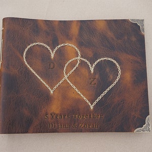 May include: A brown leather photo album with two stitched hearts, the initials "D" and "Z" inside the hearts, and the text "5 Years Together Dijana & Zoran".