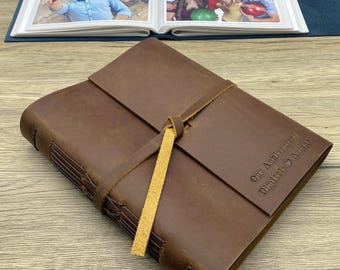 Könnte beinhalten: Ein braunes, ledergebundenes Tagebuch mit einer gelben Schleife zum Verschließen. Das Tagebuch trägt eine personalisierte Inschrift mit dem Text "Unser Jahrestag, Daniel & Ariana".