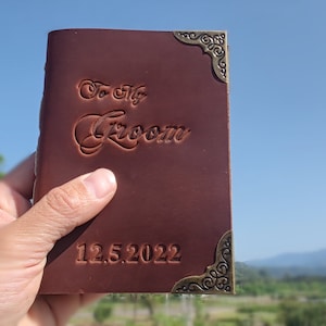 May include: A brown leather journal with a decorative brass corner piece. The journal has the words "To My Groom" embossed on the front cover and the date "12.5.2022" embossed below.