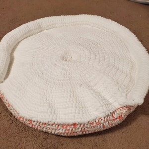 May include: A white crocheted round cushion with a pink and white crocheted border.