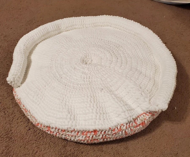 May include: A white crocheted round cushion with a pink and white crocheted border.