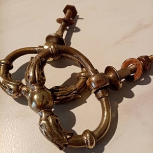 Könnte beinhalten: Zwei antike Messing-Türgriffe mit verzierten Details und einem dekorativen Ring. Die Griffe sind an Metallstangen mit Schrauben befestigt.