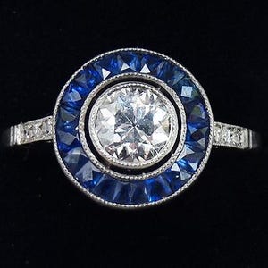 May include: A silver ring featuring a large round diamond encircled by a halo of blue sapphires.