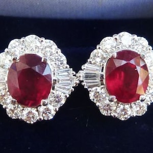 May include: A pair of ruby and diamond earrings. Each earring features a large oval-shaped ruby surrounded by a halo of smaller diamonds.