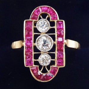 May include: A gold ring with a geometric design featuring three round diamonds and a border of square-cut rubies.
