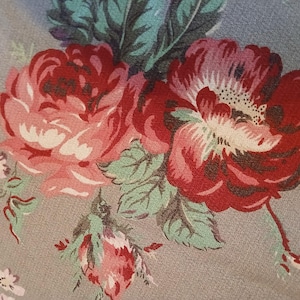 May include: A close-up of a floral pattern featuring large, red and pink roses with white centers and green leaves. The flowers are set against a muted grey background, creating a vintage aesthetic. The design is reminiscent of classic floral textiles.