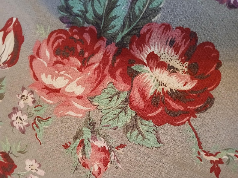 May include: A close-up of a floral pattern featuring large, red and pink roses with white centers and green leaves. The flowers are set against a muted grey background, creating a vintage aesthetic. The design is reminiscent of classic floral textiles.