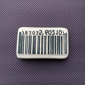 Könnte beinhalten: Ein rechteckiger weißer Gummistempel mit schwarzer Tinte. Der Stempel trägt den Text "L09032 8S" und einen Barcode.