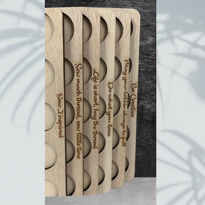 May include: Wooden storage box with multiple compartments for thread spools. The box has a light wood finish and is engraved with inspirational quotes about sewing.