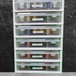 May include: A white plastic drawer unit with six clear drawers. Each drawer has a label with the text "SACORD Drawer" and a number, followed by a range of numbers. For example, the top drawer is labeled "SACORD Drawer 1 0003-0250".