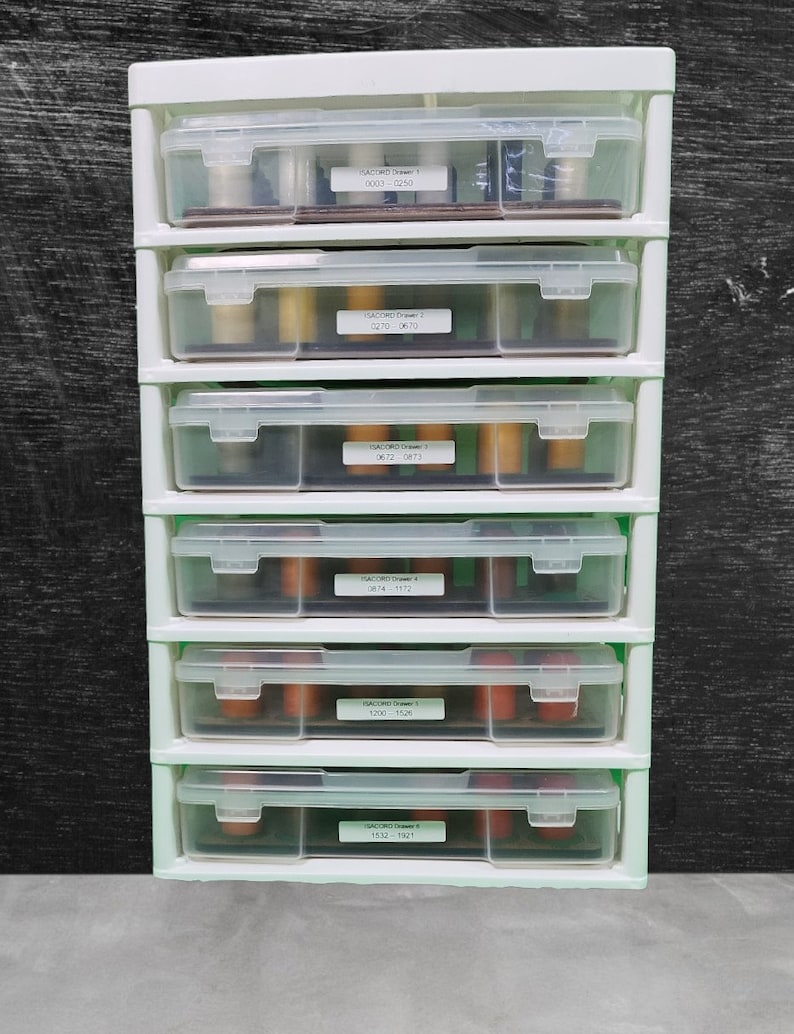 May include: A white plastic drawer unit with six clear drawers. Each drawer has a label with the text "SACORD Drawer" and a number, followed by a range of numbers. For example, the top drawer is labeled "SACORD Drawer 1 0003-0250".