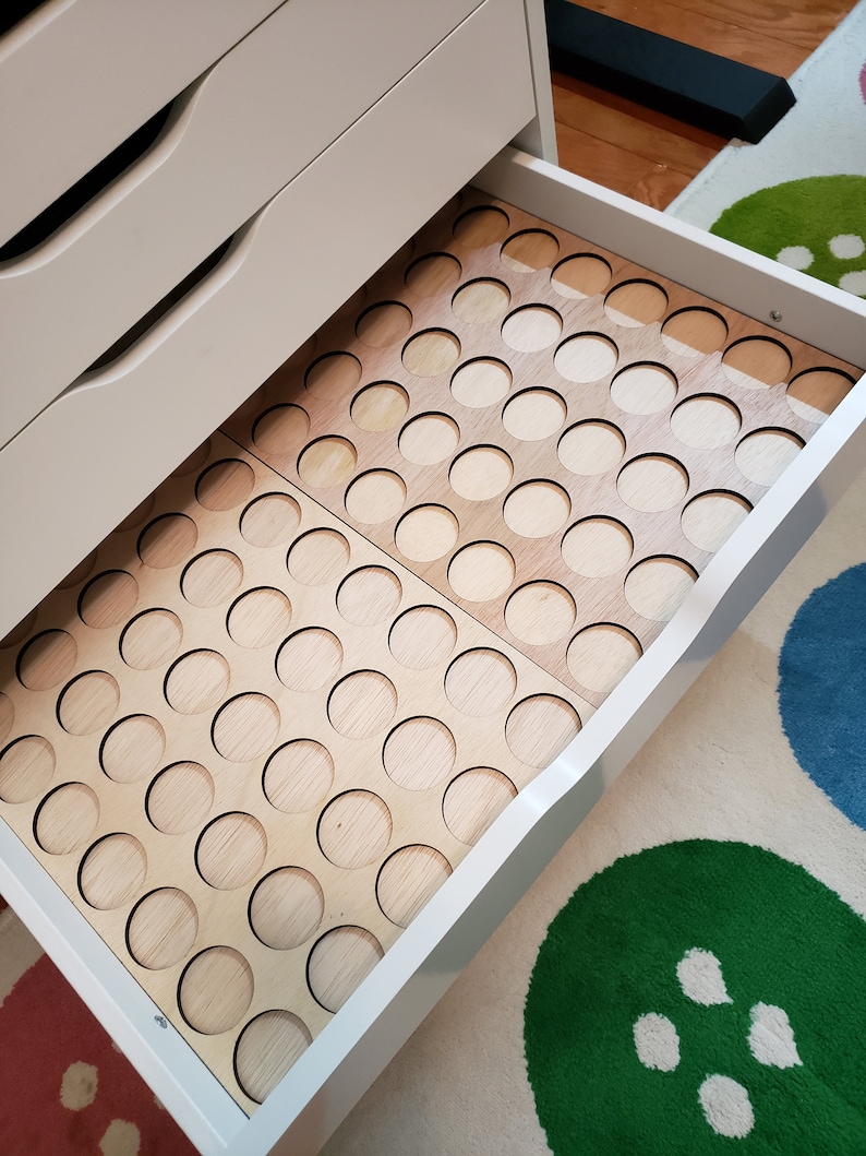 May include: A white drawer with a wooden insert that has a grid of circular cutouts. The drawer is open and the insert is visible. The insert is made of light wood and has a natural finish.
