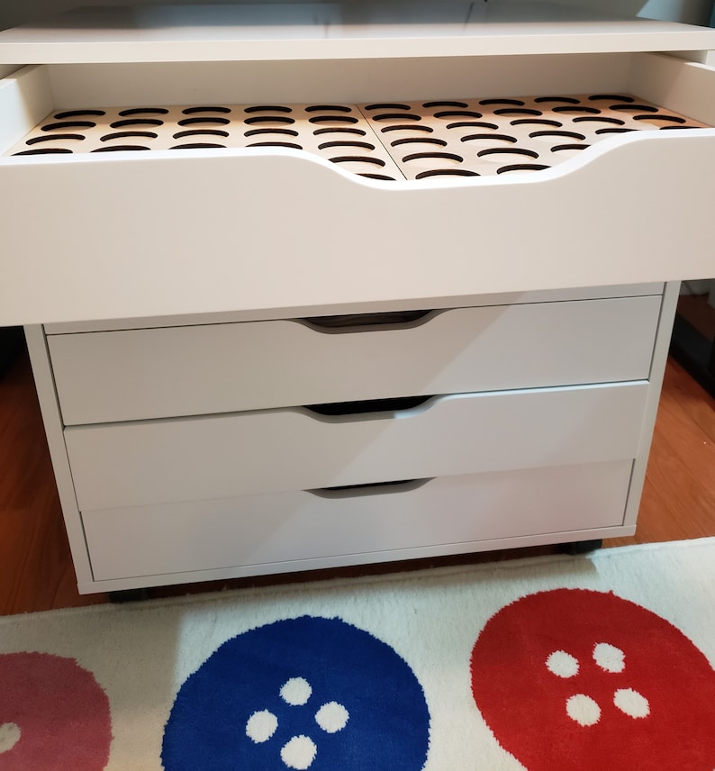 May include: White rolling storage cabinet with four drawers. The top drawer is open and has a wooden insert with multiple circular compartments.