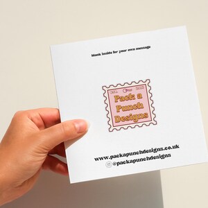 A hand holding a white card with text and an image of a stamp.