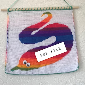 Puede incluir: Un tapiz de pared tejido con un diseño de gusano arcoíris sobre un fondo blanco. El gusano tiene ojos saltones. El texto "PDF FILE" está en un rectángulo blanco. La pieza se cuelga de un palito de madera con una cuerda verde.