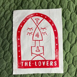May include: Red and white printed fabric with a design of a stylised face with eyes closed, a number 4, and the text "THE LOVERS".