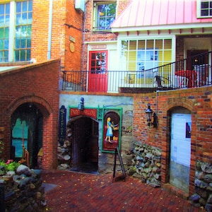 May include: A brick building with a red roof and a black metal railing. There is a sign that says "Paddy's Saloon" and a door with a sign that says "Restaurant".