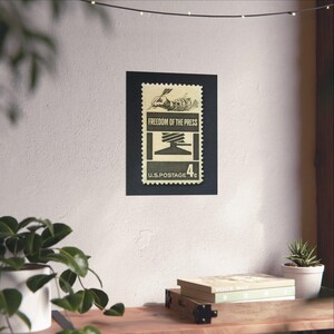 May include: A vintage US postage stamp with a black and white illustration of a hand holding a pen and a printing press. The stamp reads "Freedom of the Press" and "U.S. Postage 4&cent;".