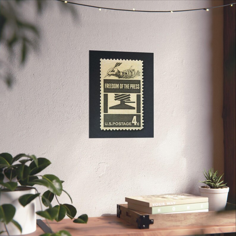 May include: A vintage US postage stamp with a black and white illustration of a hand holding a pen and a printing press. The stamp reads "Freedom of the Press" and "U.S. Postage 4&cent;".
