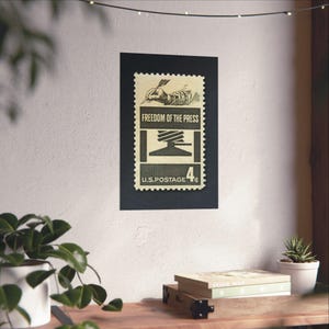 May include: A vintage US postage stamp with a black and white illustration of a printing press and a hand holding a pen. The stamp is beige with black text that reads "Freedom of the Press" and "U.S. Postage 4&cent;".