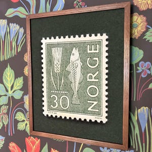 May include: A framed wall art piece featuring a vintage Norwegian postage stamp design. The stamp is cream-coloured with dark green ink, depicting a fish, a stalk of grain, the number 30, and the text NORGE, all set against a dark green mat.