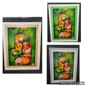 Puede incluir: Una pintura de diamantes enmarcada con dos personajes de Pokémon, Pikachu y Eevee, sobre un fondo verde. La pintura está en un marco blanco con un passe-partout crema.