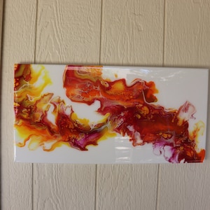 May include: Abstract painting with swirling red, orange, and yellow paint on a white background.