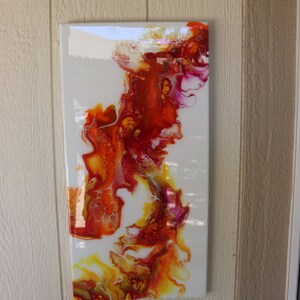 May include: Abstract painting on canvas with swirling red, orange, and yellow paint on a white background.