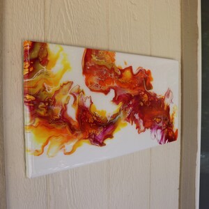 May include: Abstract painting with swirling yellow, orange, red, and pink paint on a white background.