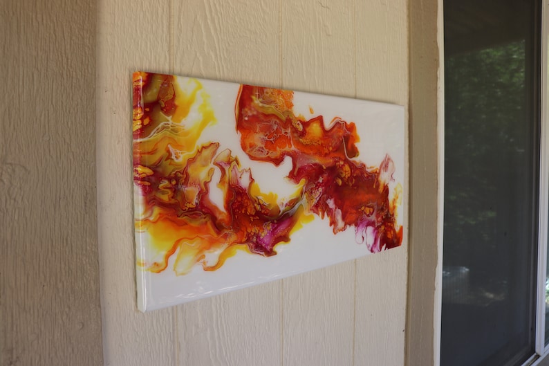 May include: Abstract painting with swirling yellow, orange, red, and pink paint on a white background.