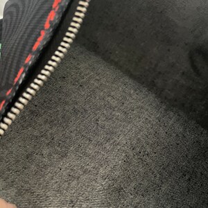 May include: Black zippered pouch with a red and black patterned lining. The pouch is made of a soft, textured fabric.