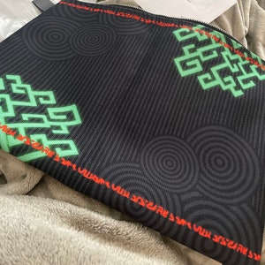 May include: Black zippered pouch with a green and red geometric pattern. The pattern features repeating circles and a stylized design.
