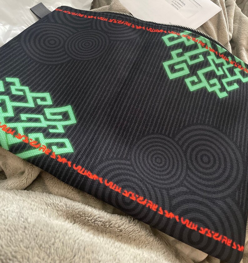 May include: Black zippered pouch with a green and red geometric pattern. The pattern features repeating circles and a stylized design.