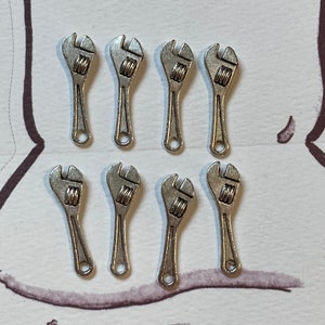 May include: Eight silver-toned miniature adjustable wrenches, arranged in two rows of four, on a white background.