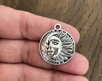 May include: Silver charm featuring a detailed sun and moon design. The sun has a face and rays, while the moon is a crescent shape.