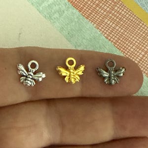 May include: Three bee charms in different finishes: silver, gold, and antique silver. The charms are small and delicate, perfect for adding a touch of whimsy to jewelry or crafts.