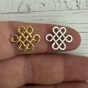 May include: Two metal charms in the shape of a knot, one gold and one silver. The charms are on a finger.