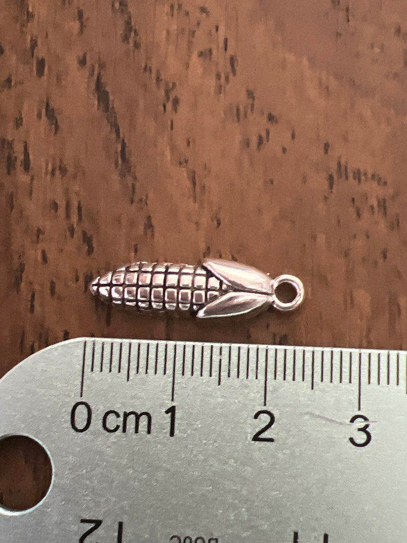 May include: Silver charm in the shape of an ear of corn, measuring approximately 1.5 cm in length.