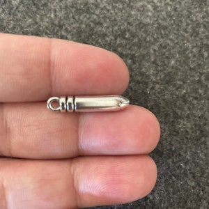 May include: A silver bullet charm with a loop at the top for attaching to a necklace or bracelet.
