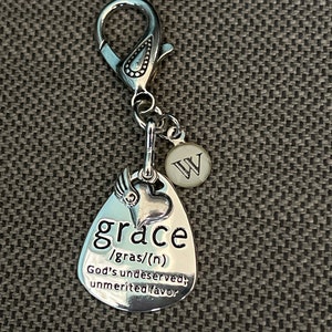 May include: Silver charm with a heart and the word "grace" defined as "God's undeserved, unmerited favor". The charm is attached to a silver clip with a letter "W" charm.
