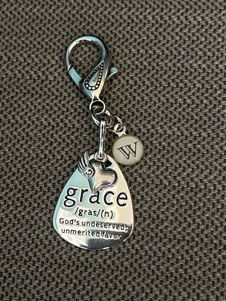 May include: Silver charm with a heart and the word "grace" defined as "God's undeserved, unmerited favor". The charm is attached to a silver clip with a letter "W" charm.